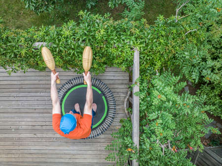 senior man is exercising with wooden Indian clubs on a mini trampoline in his backyard patio, top...