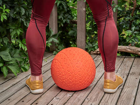 male in compression pants is exercising with a heavy slam ball on a backyard deck, functional...