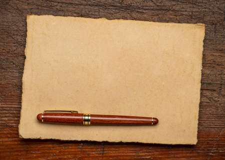 sheets of blank handmade paper with rough edges and a stylish pen against rustic weathered woodの写真素材