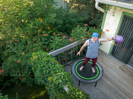 senior man is rebounding on a mini trampoline with a small medicine ball in his backyard patio, late...