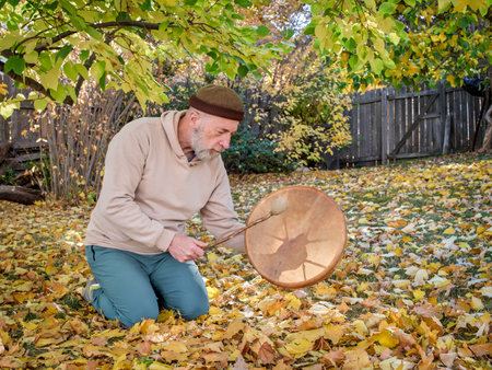 senior man is sitting in seiza position and  playing a shaman drum in a fall sceneryの写真素材