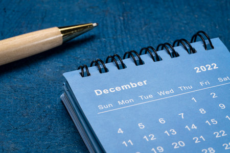 December 2022 - spiral desktop calendar against blue textured paper with a stylish pen, low angle shot, time and business conceptの写真素材