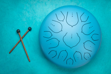 blue steel tongue drum with mallets, top view against textured paper background