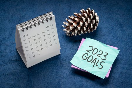 2023 goals  - handwriting in black ink on a reminder note with a January desktop calendar and frosty pine cone, New Year goals and resolutions conceptの写真素材