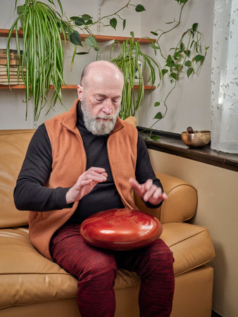 focused senior man is playing steel tongue drum with his hands, lifestyle and hobby concept