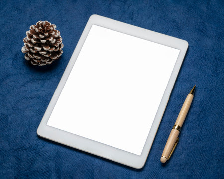 mockup of digital tablet with a blank isolated screen, flat lay with a frosty pine cone on blue...