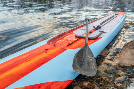 racing stand up paddleboard with paddle, safety leash and steering system on a lake shore, fitness and training conceptの写真素材