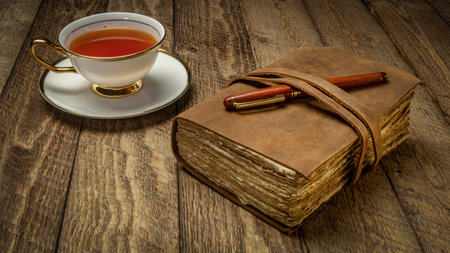 antique leatherbound journal with a cup of tea and pen on a rustic wooden tableの写真素材
