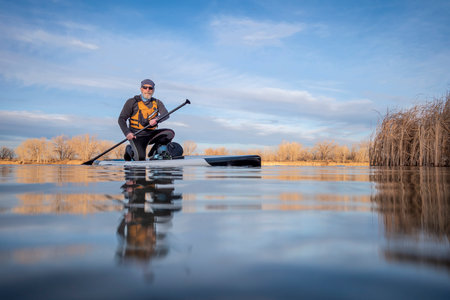 senior paddler and his paddleboard on lake in winter or early spring in Colorado, frog perspective (partially submerged action camera)の写真素材