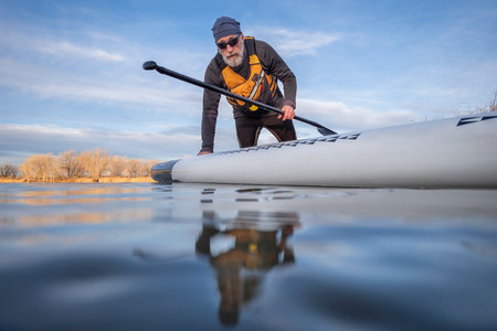 senior paddler and his paddleboard on lake in winter or early spring in Colorado, frog perspective (partially submerged action camera)の写真素材