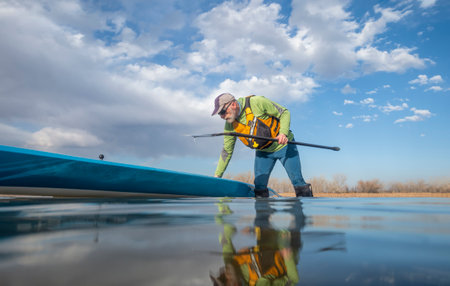 senior paddler and his paddleboard on lake in winter or early spring in Colorado, frog perspective (partially submerged action camera)の写真素材