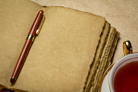 blank retro leather-bound journal with decked edge handmade paper pages with a stylish pen and a cup of tea, journaling conceptの写真素材