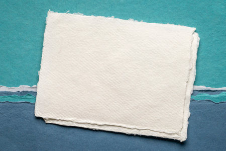 small sheet of blank white Khadi rag paper from India against abstract landscape in blue tonesの写真素材