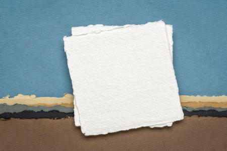 small sheet of blank white Khadi rag paper from India against abstract landscape in earth pastel tonesの写真素材