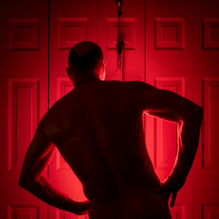 silhouette of a senior athletic, man torso standing in front of the red light therapy panel, home setup for treatmentの写真素材