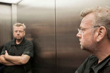 Man in the elevator looking at himself skeptically in the mirrorの写真素材