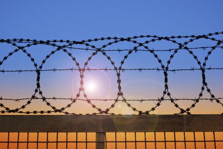 Behind a barbed wire fence, the sun goes downの写真素材