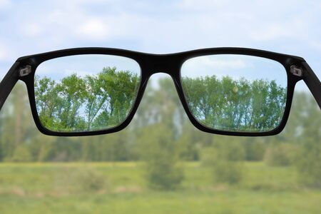 Black glasses in front of green landscape, sharpness can only be seen in the lensesの写真素材