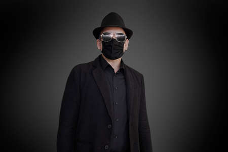 A fashion-conscious man in a black suit, face mask, hat and sunglassesの写真素材