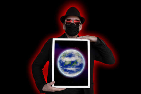 A man with a face mask holds a picture frame in front of his chest in which the earth can be seen