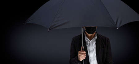 A man with a mask holds a black umbrellaの写真素材