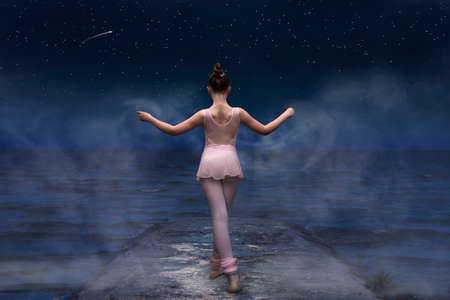A young woman is dancing ballet by the sea, the sky is clear with starsの写真素材