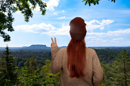 A red-haired woman stands on a mountain and makes the victory sign with her handの写真素材