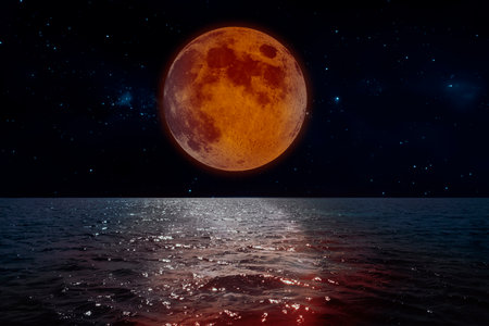 The red full moon is reflected in the ocean waves on the starry nightの写真素材