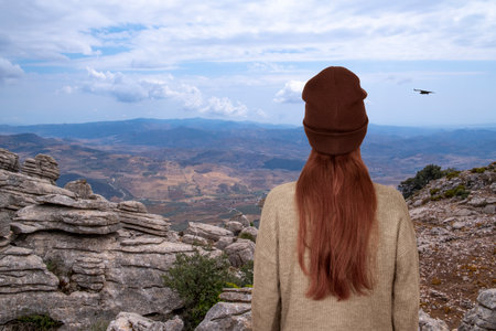 A red-haired girl stands in front of an impressive mountain landscape in Spainの写真素材