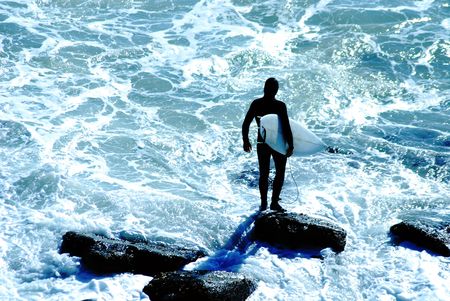 Surfer in wetsuit holds tightly onto his surfboard before jumping into the cold Pacific Ocean in Malibu, California.の写真素材