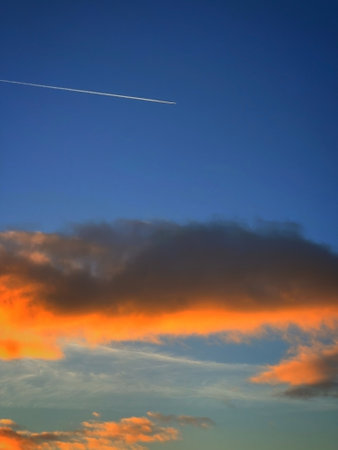 Airplane trace in the blue sky at sunsetの写真素材