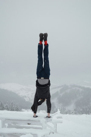 A man does a handstand on top of a mountain in winter