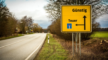 An image with a signpost pointing in two different directions in German. One direction points to Cheap, the other points to Expensive.の写真素材