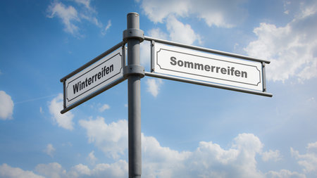 An image with a signpost pointing in two different directions in German. One direction points to summer tires, the other points to winter tires.の写真素材