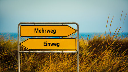 An image with a signpost pointing in two different directions in German. One direction points to reusable the other points to one way.の写真素材