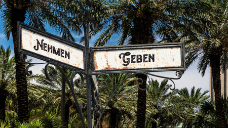 An image with a signpost pointing in two different directions in German. One direction points to give, the other points to take.の写真素材