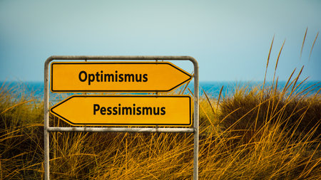 An image with a signpost pointing in two different directions in German. One direction points to optimism, the other points to pessimism.の写真素材