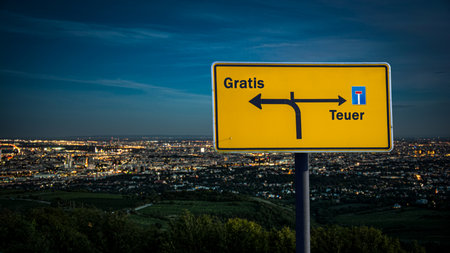 An image with a signpost pointing in two different directions in German. One direction points to Free, the other points to Expensive.の写真素材