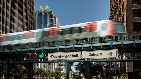 An image with a signpost pointing in two different directions in German. One direction points to the future, the other points to the past.の写真素材