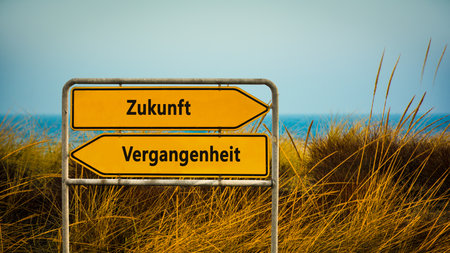An image with a signpost pointing in two different directions in German. One direction points to the future, the other points to the past.の写真素材