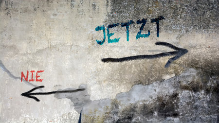 An image with a signpost pointing in two different directions in German. One direction is now, the other is never.の写真素材