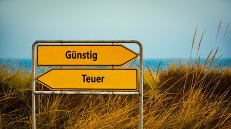An image with a signpost pointing in two different directions in German. One direction points to Cheap, the other points to Expensive.の写真素材