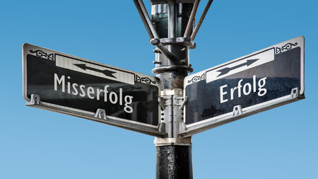 An image with a signpost pointing in two different directions in German. One direction points to success, the other points to failure.の写真素材