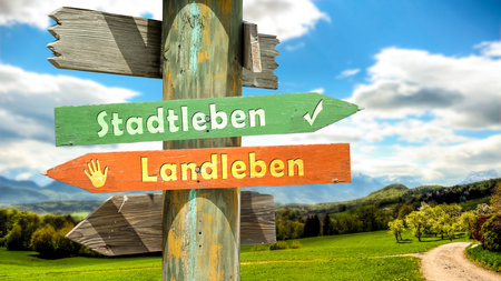 An image with a signpost pointing in two different directions in German. One direction points to city life, the other points to country life.の写真素材