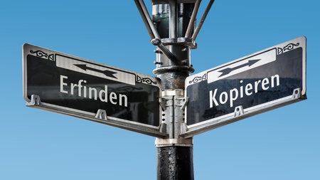 An image with a signpost pointing in two different directions in German. One direction is copying, the other is invention.の写真素材