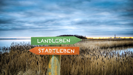 An image with a signpost pointing in two different directions in German. One direction points to country life, the other points to city life.の写真素材