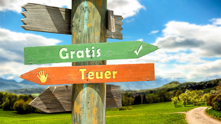 An image with a signpost pointing in two different directions in German. One direction points to Free, the other points to Expensive.の写真素材