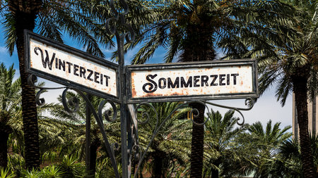 An image with a signpost pointing in two different directions in German. One direction shows Daylight Saving Time, the other shows Winter Time.の写真素材