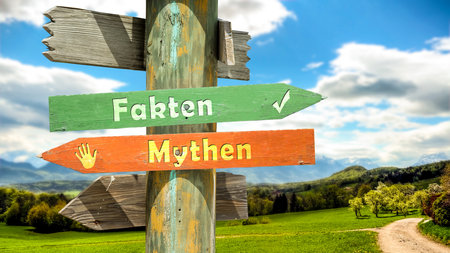 An image with a signpost pointing in two different directions in German. One direction points to facts, the other points to myths.の写真素材