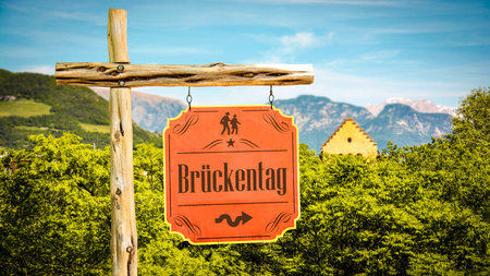 picture shows a sign post and a sign pointing to bridge day in german.の写真素材